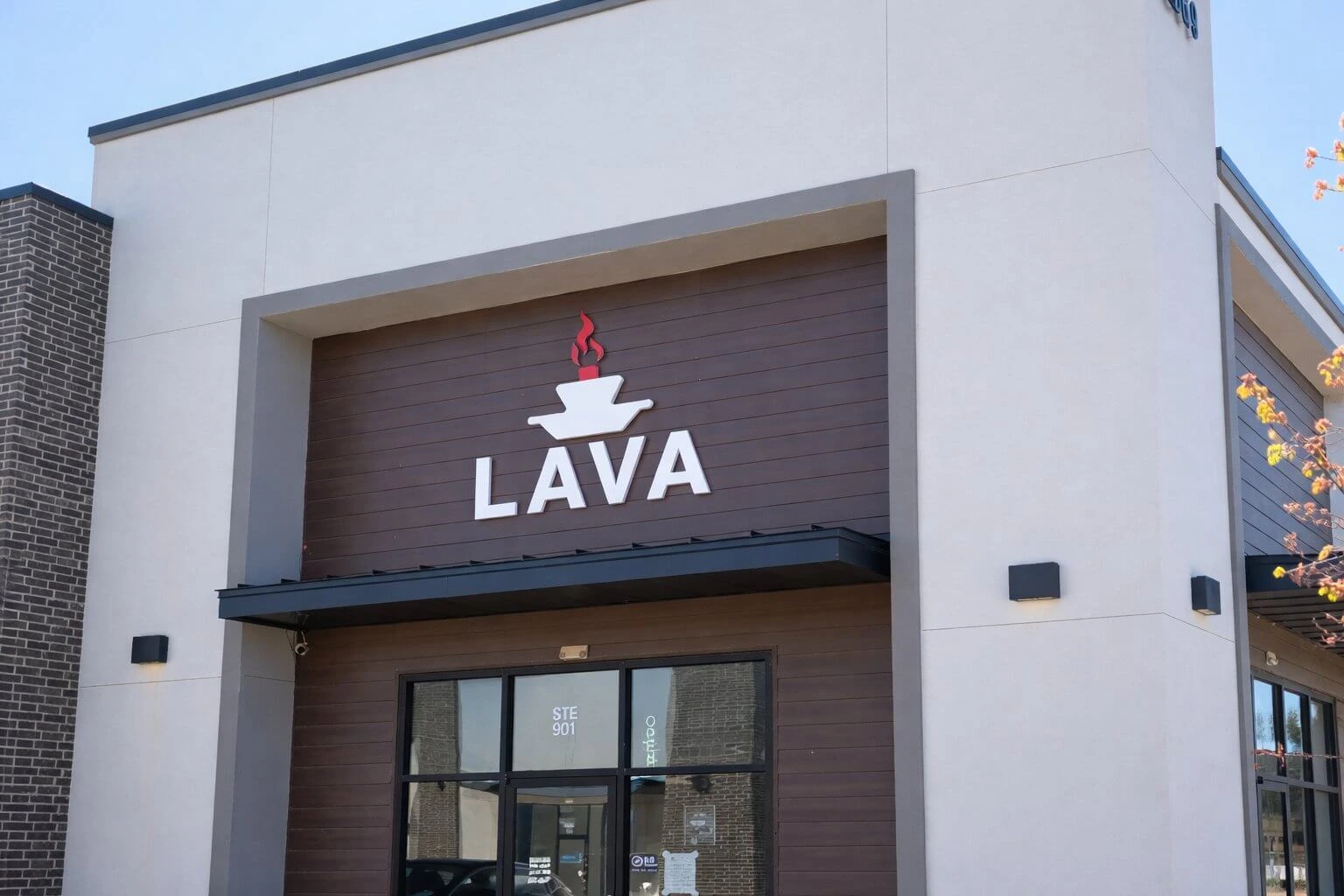 LAVA storefront entrance in daylight, white dimensional letters and colour mark mounted above the glass door on a dark wood panel facade