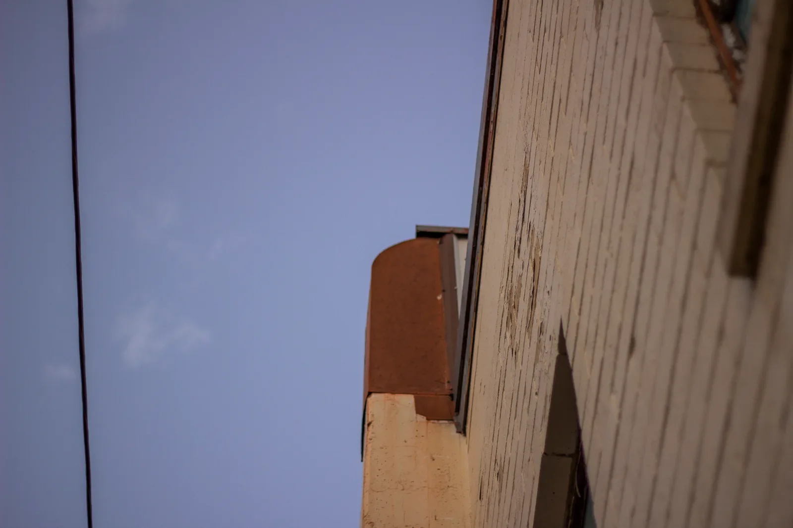 A sharp upward view of the corner of the school building against a deep blue sky, a single power line cutting across