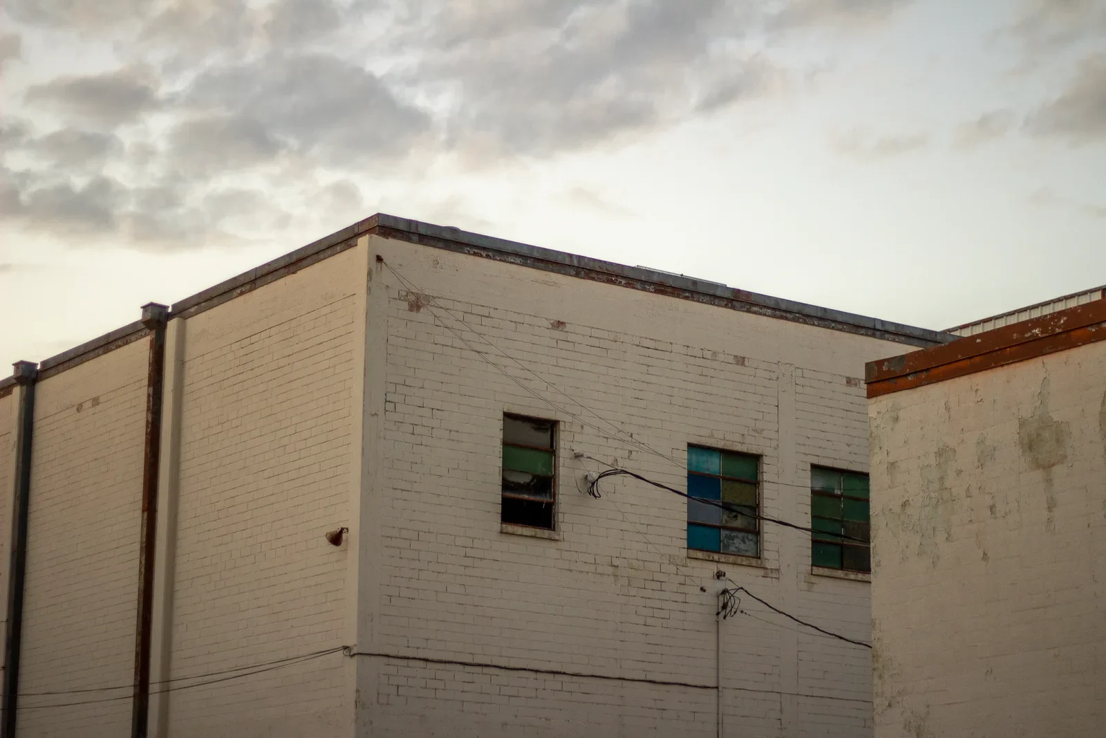 The corner of a cream brick gymnasium against a cloud-streaked evening sky, small windows high on the wall