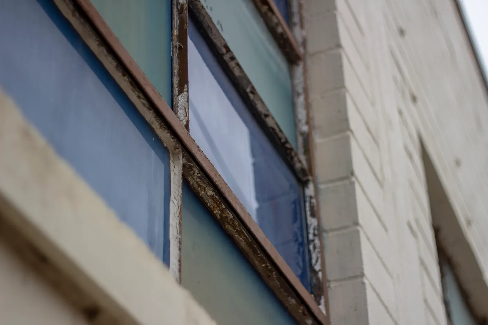 A steep upward view along a band of gymnasium windows, teal and white painted panels catching the light