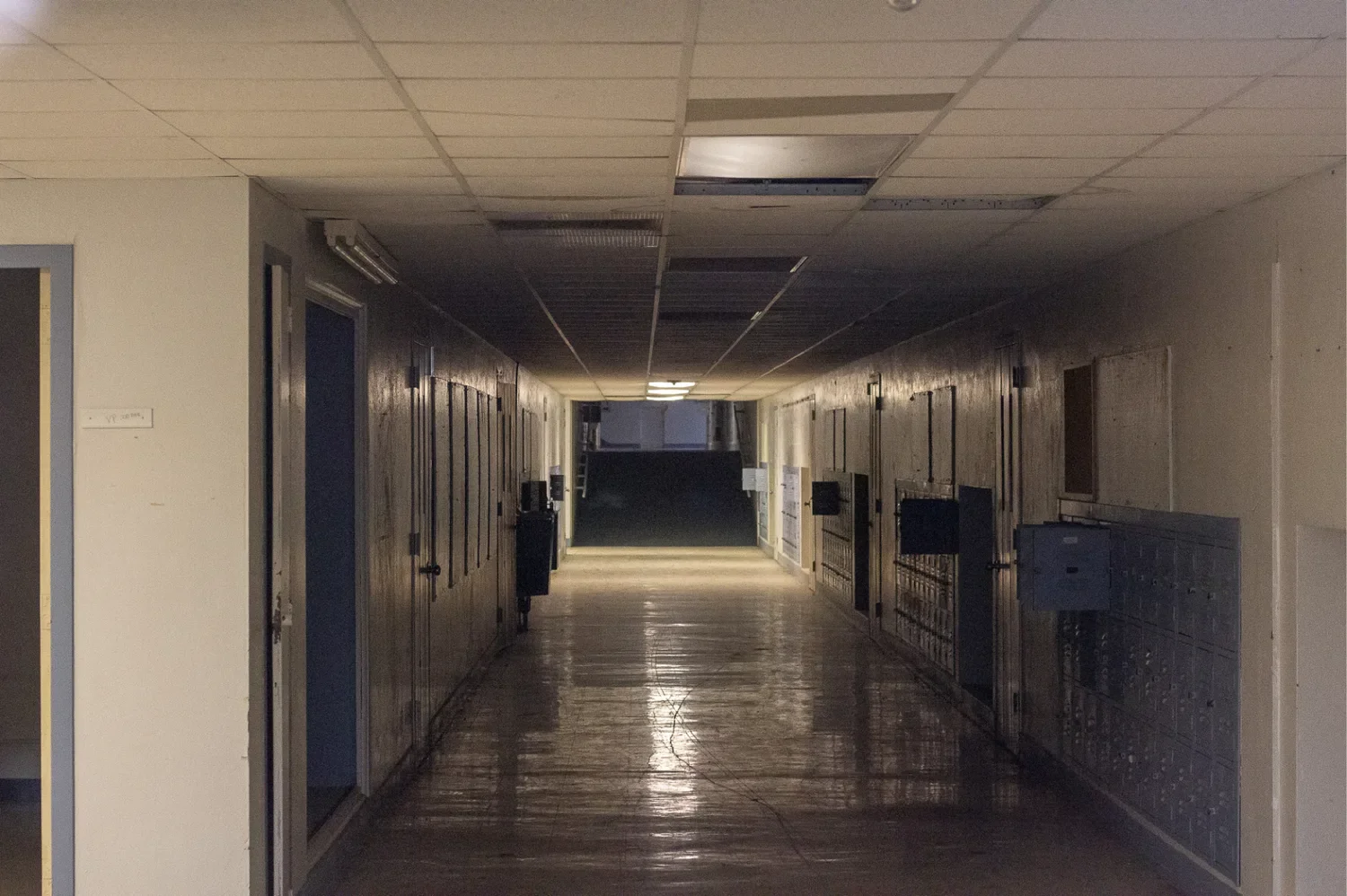 A long empty school corridor with lockers down the right wall, receding to a bright doorway at the far end