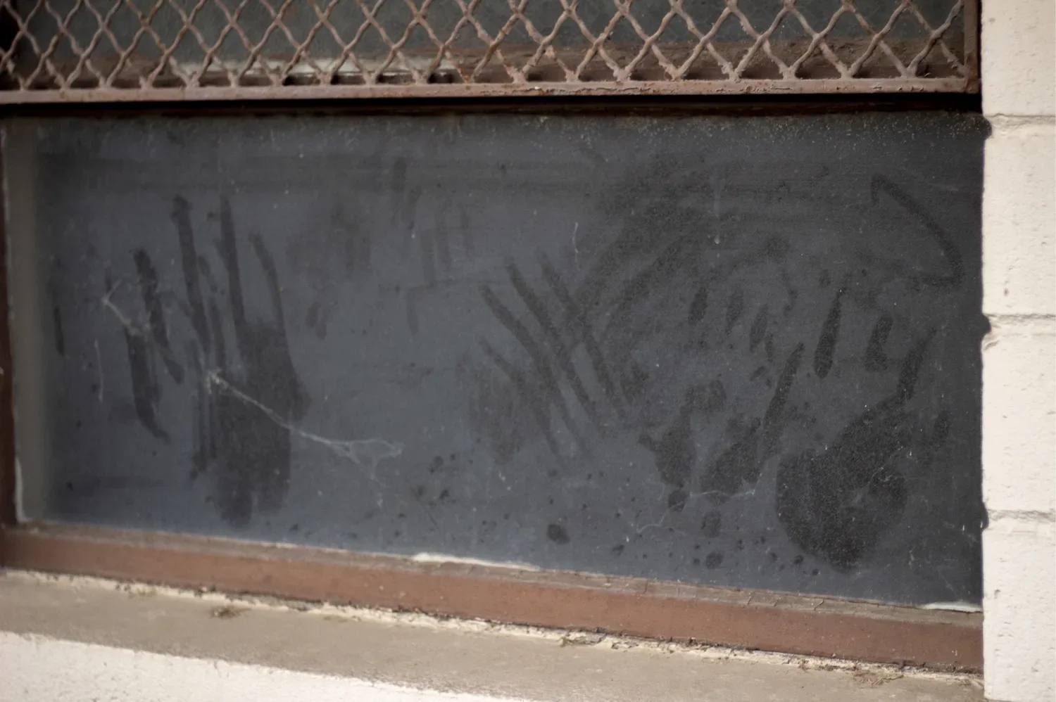 Two smeared handprints on a filthy window pane, the dark interior of a classroom barely visible behind the glass