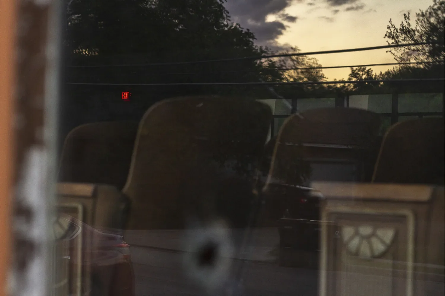 Rows of upholstered auditorium seats seen through a window, with sunset sky and power lines reflected across the glass